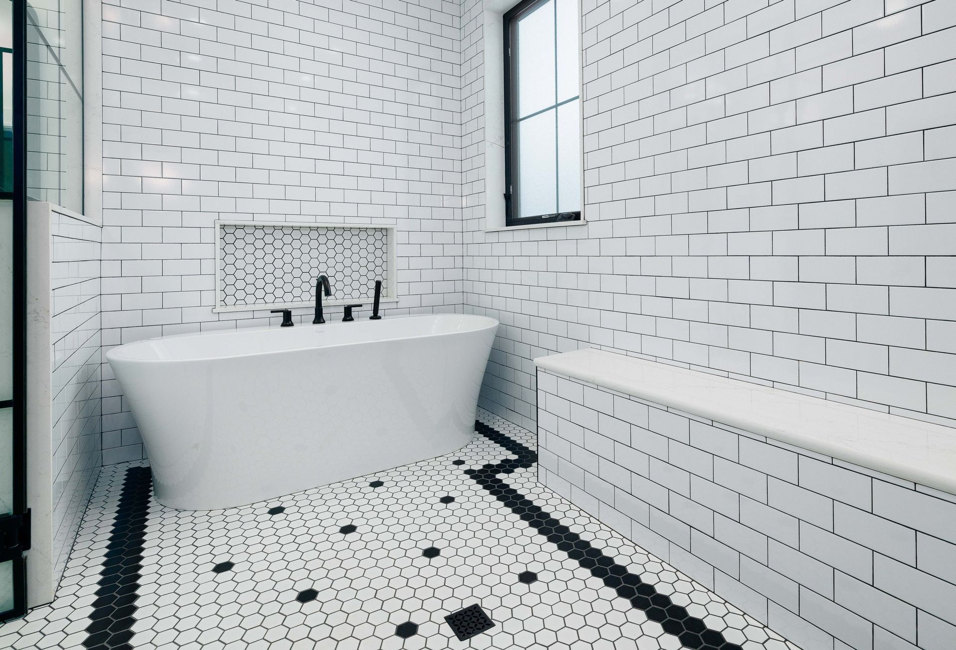 A modern bathroom with a white freestanding tub, black fixtures, white subway-tiled walls, and patterned tile flooring.