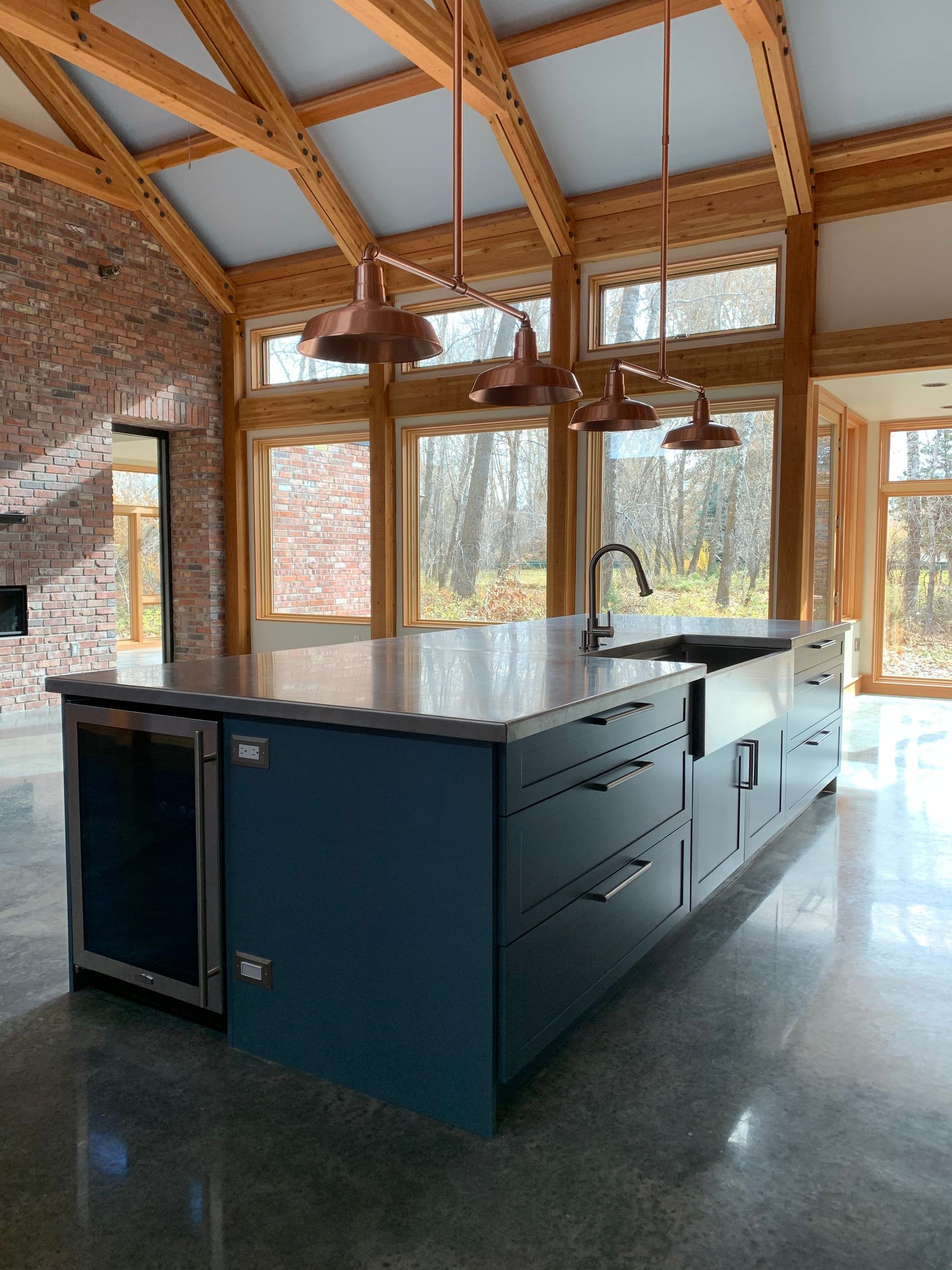 A modern kitchen island with a dark blue base, stainless steel sink, and wine cooler under warm pendant lights.