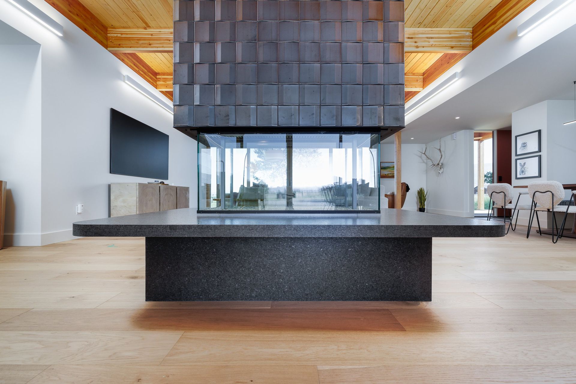 A modern living room features a large, central glass fireplace with a textured dark grey surround and a stone base.