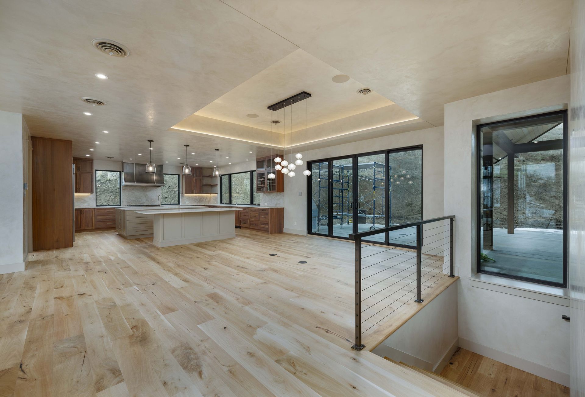 A bright, open-plan kitchen and living area with light wood floors, a large central island, and floor-to-ceiling windows.