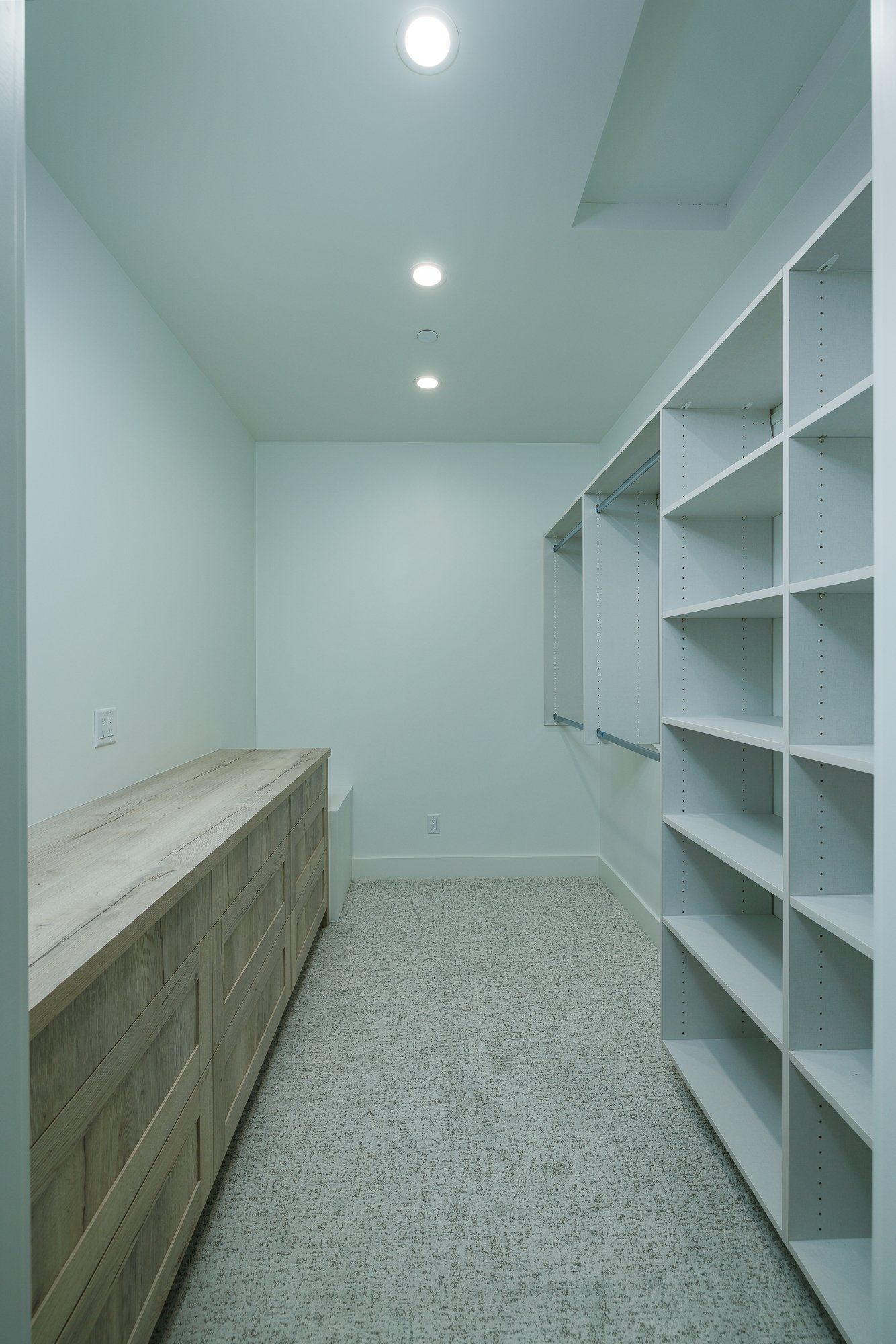 A walk-in closet featuring light wood drawers on the left, white shelving on the right, and a speckled stone floor.