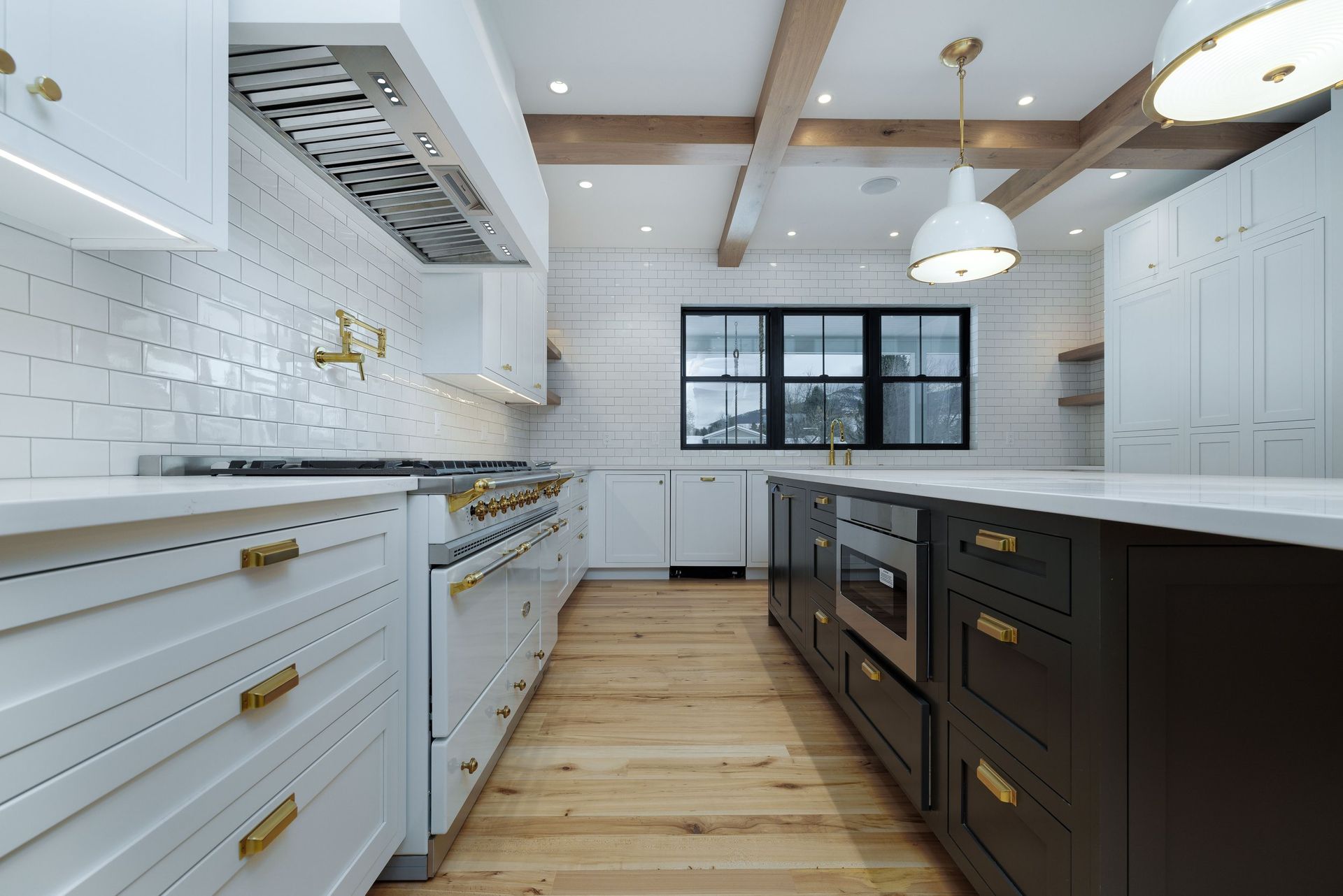 A modern kitchen with white subway tile, a dark island, light wood flooring, and gold hardware.