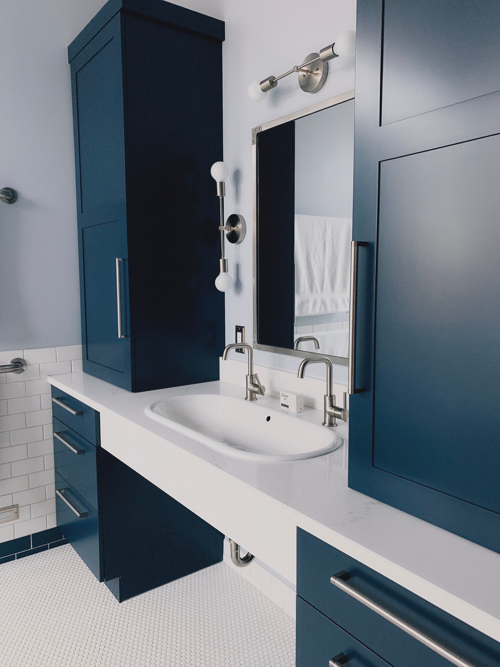 A modern bathroom featuring a deep blue vanity, a white countertop with an oval sink, and a framed mirror on a light wall.