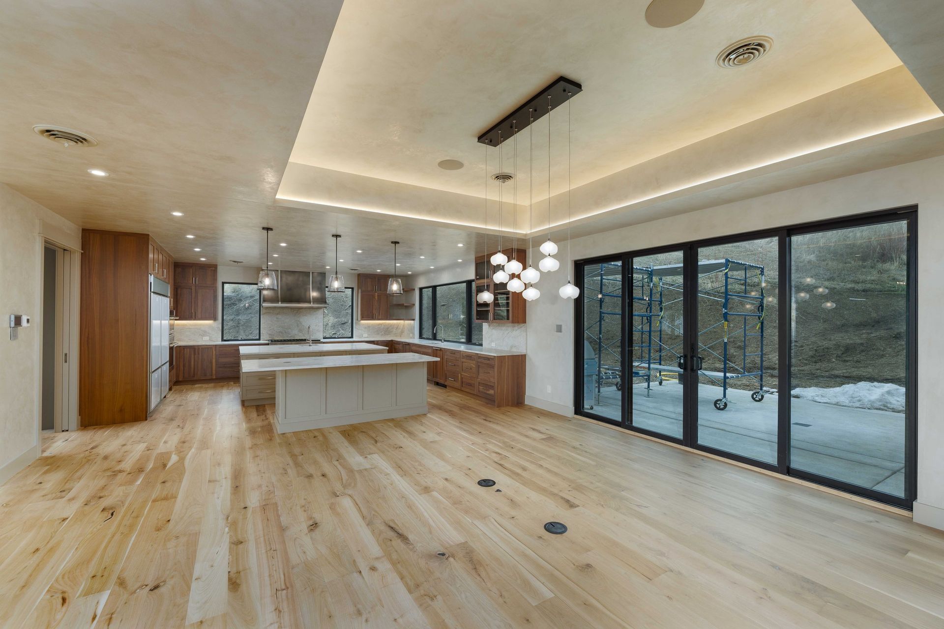 A modern, open-concept kitchen with light wood floors, white islands, dark cabinetry, and large glass sliding doors.