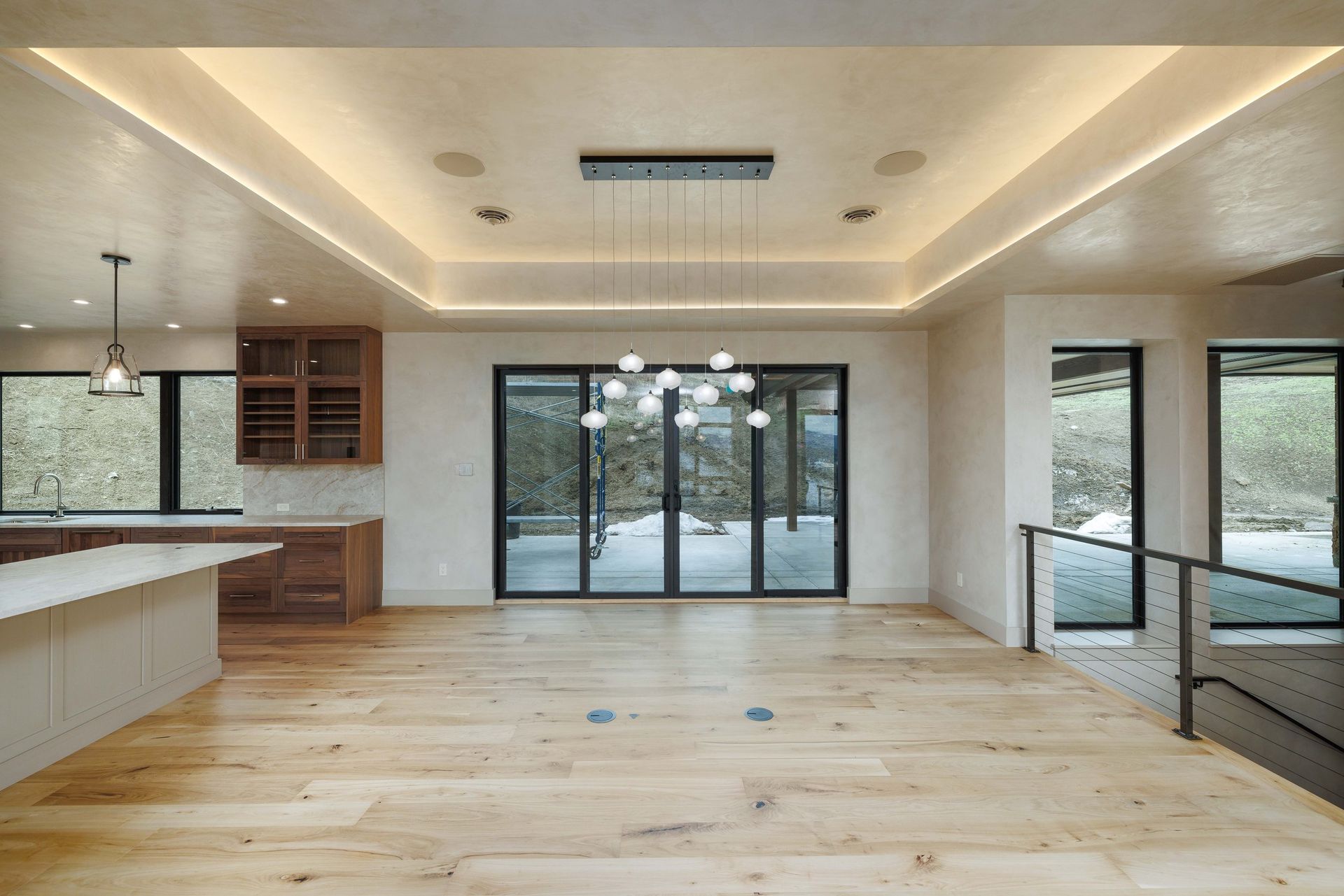 Modern dining area with wood floors, a chandelier, tray ceiling lighting, and large glass doors overlooking a landscape.