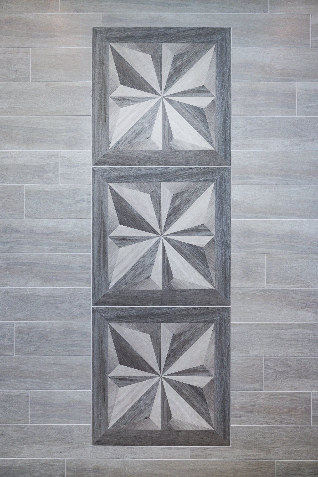 A vertical column of three square, gray geometric tiles with a starburst pattern, set within light gray wood-look tiles.