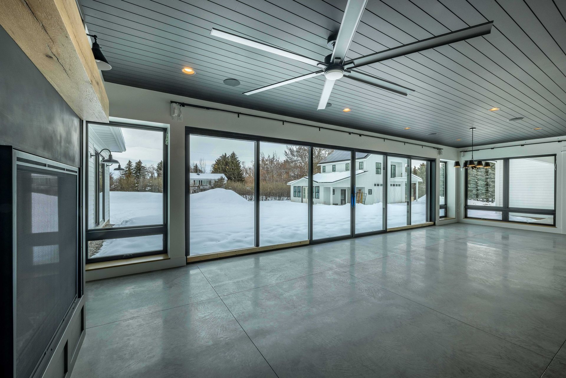 Modern living room with concrete floors, a shiplap ceiling, a large ceiling fan, and sliding glass doors showing snow.