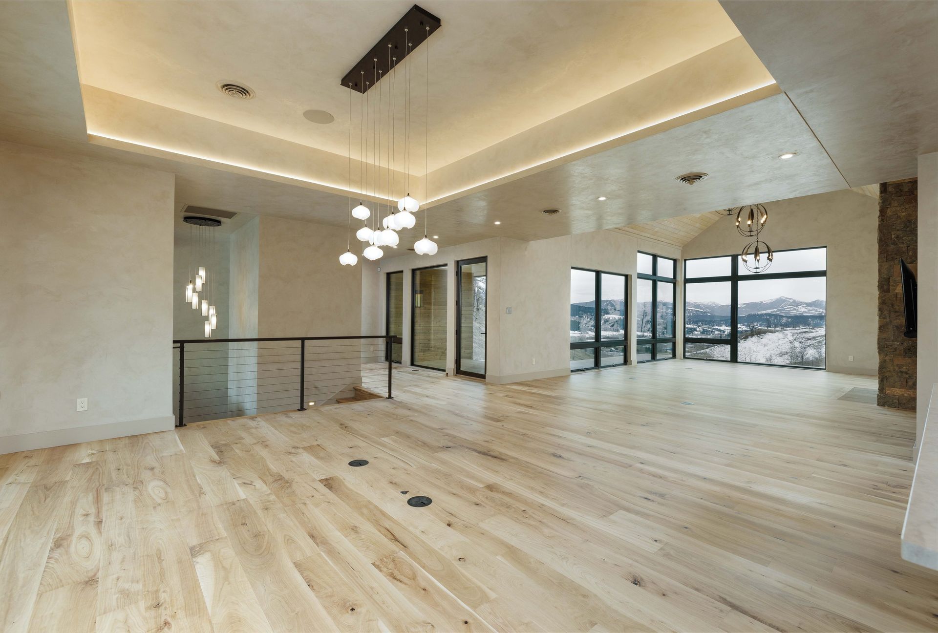 A spacious, modern interior with light wood flooring, recessed ceiling lighting, a bubble chandelier, and large windows.