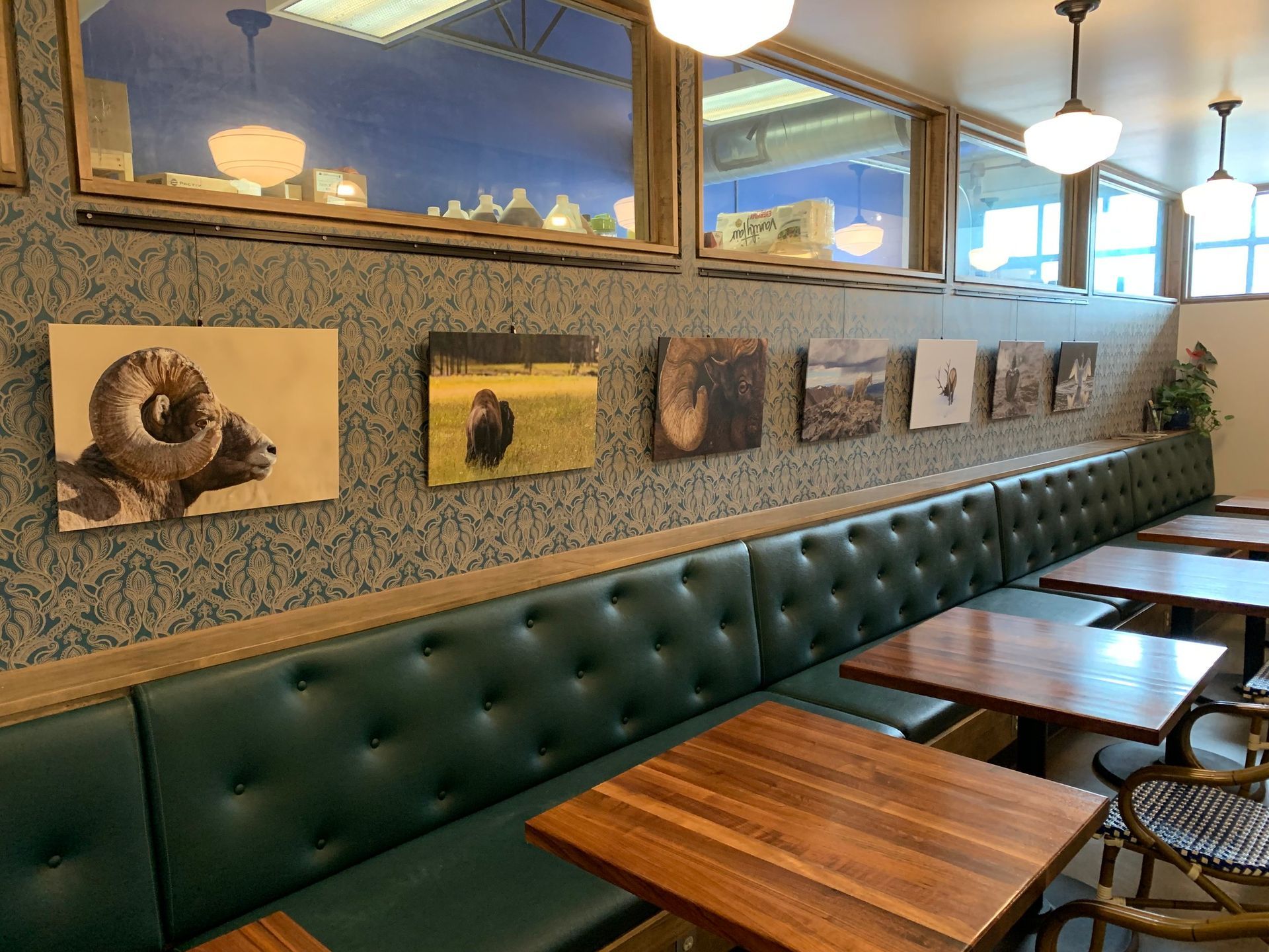 A restaurant booth with green tufted leather seating, wooden tables, and a row of nature photographs on patterned wallpaper.