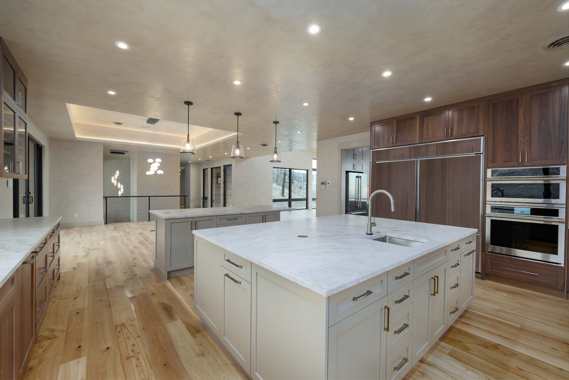A modern kitchen with a large white island, wooden cabinets, stainless steel appliances, and light wood flooring.