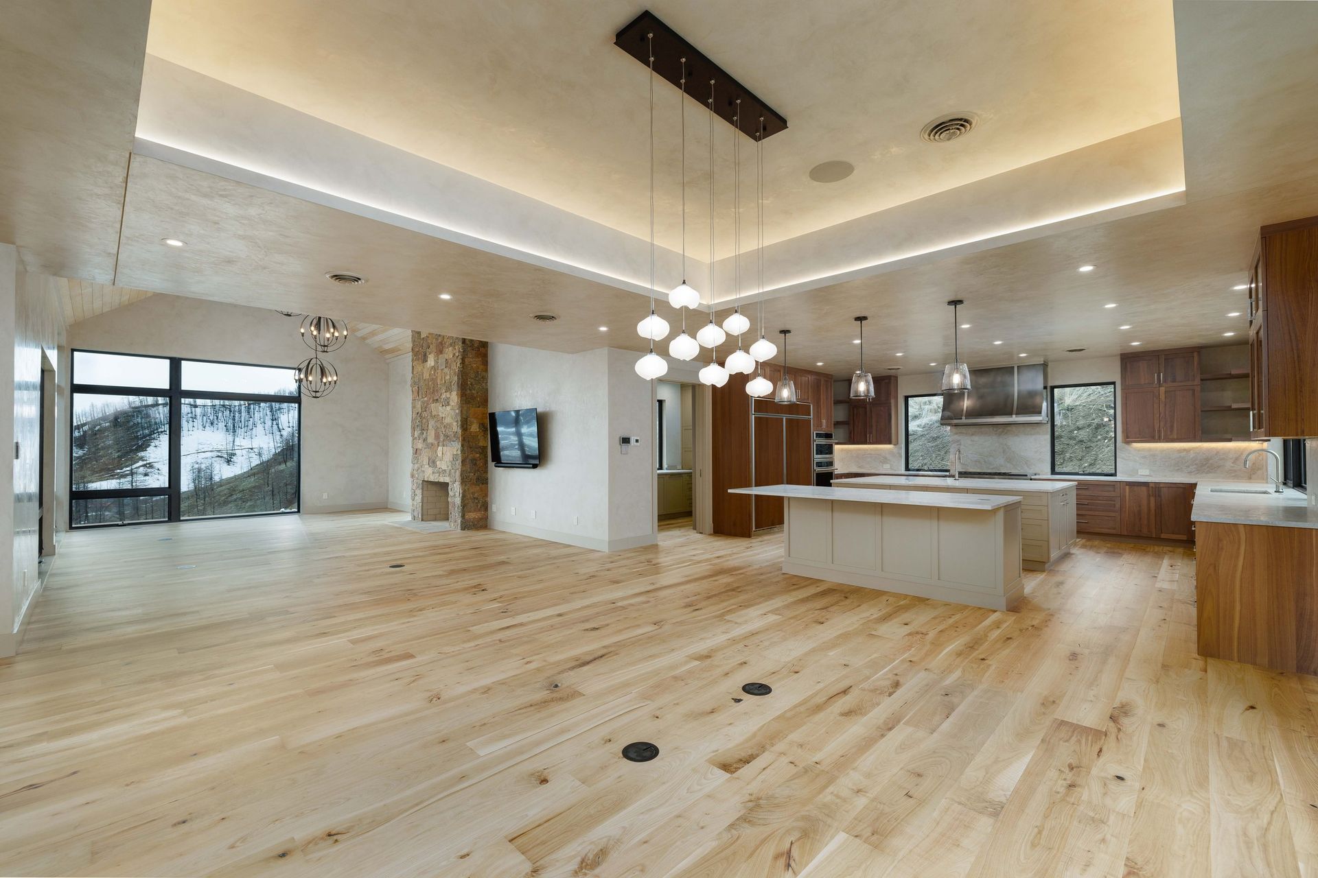 Open-concept kitchen and living area with hardwood floors, a large central island, and modern hanging light fixtures.