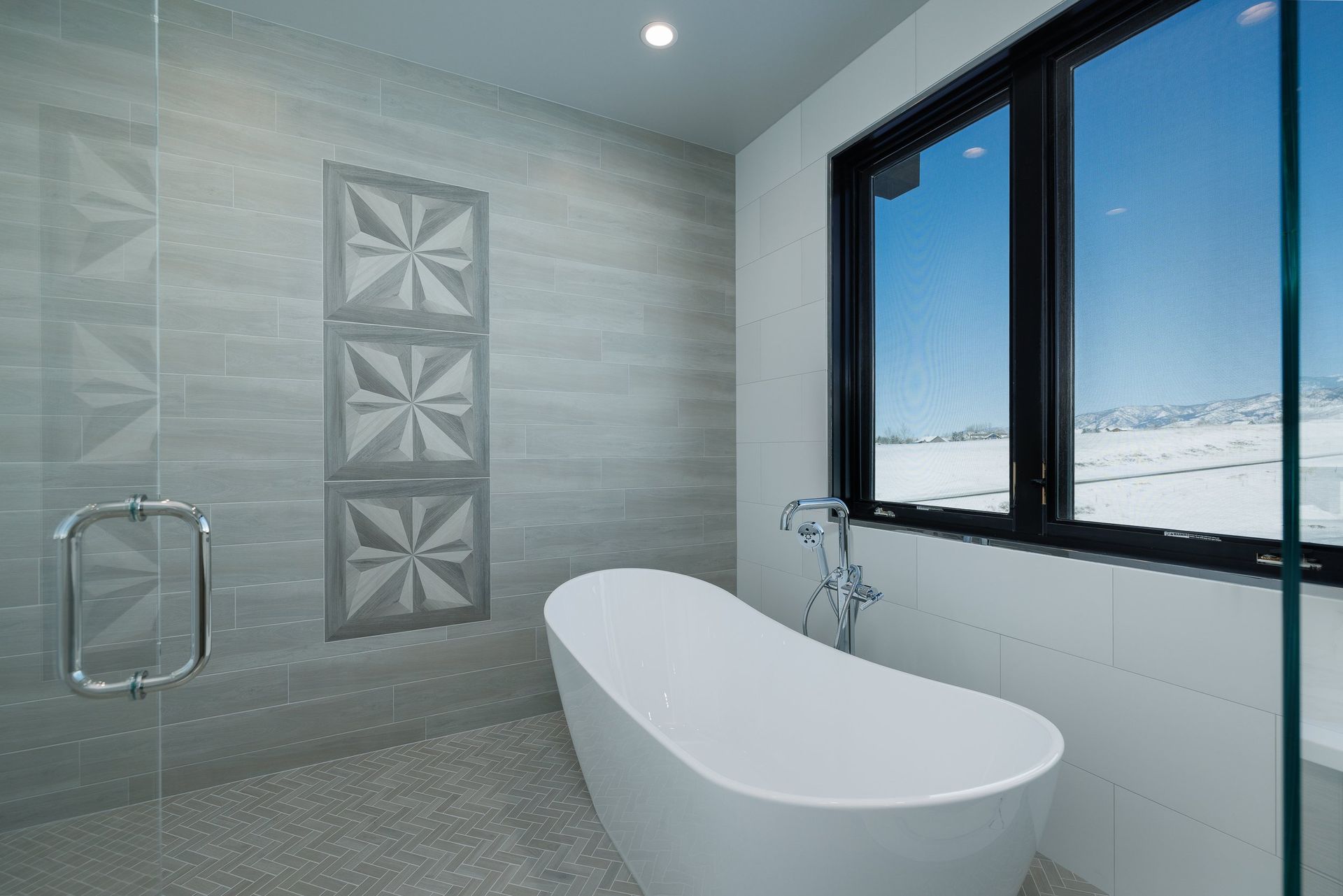 Modern bathroom featuring a white freestanding bathtub next to a large window overlooking a snowy landscape.