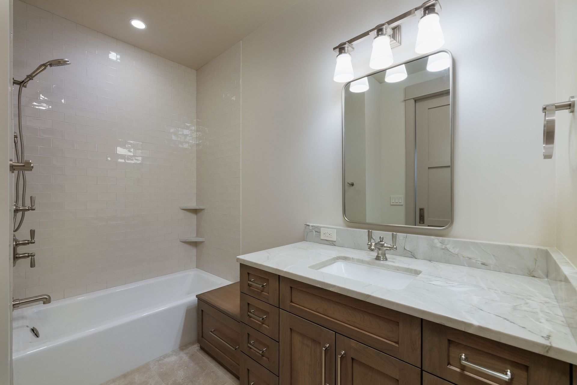 Modern bathroom with a marble vanity, wood cabinets, a wall-mounted mirror, and a combined bathtub and shower.