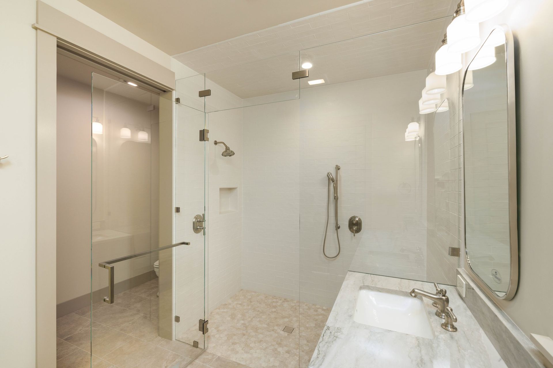 A modern bathroom with a glass-enclosed shower, stone tile flooring, and a marble vanity with a mirror.