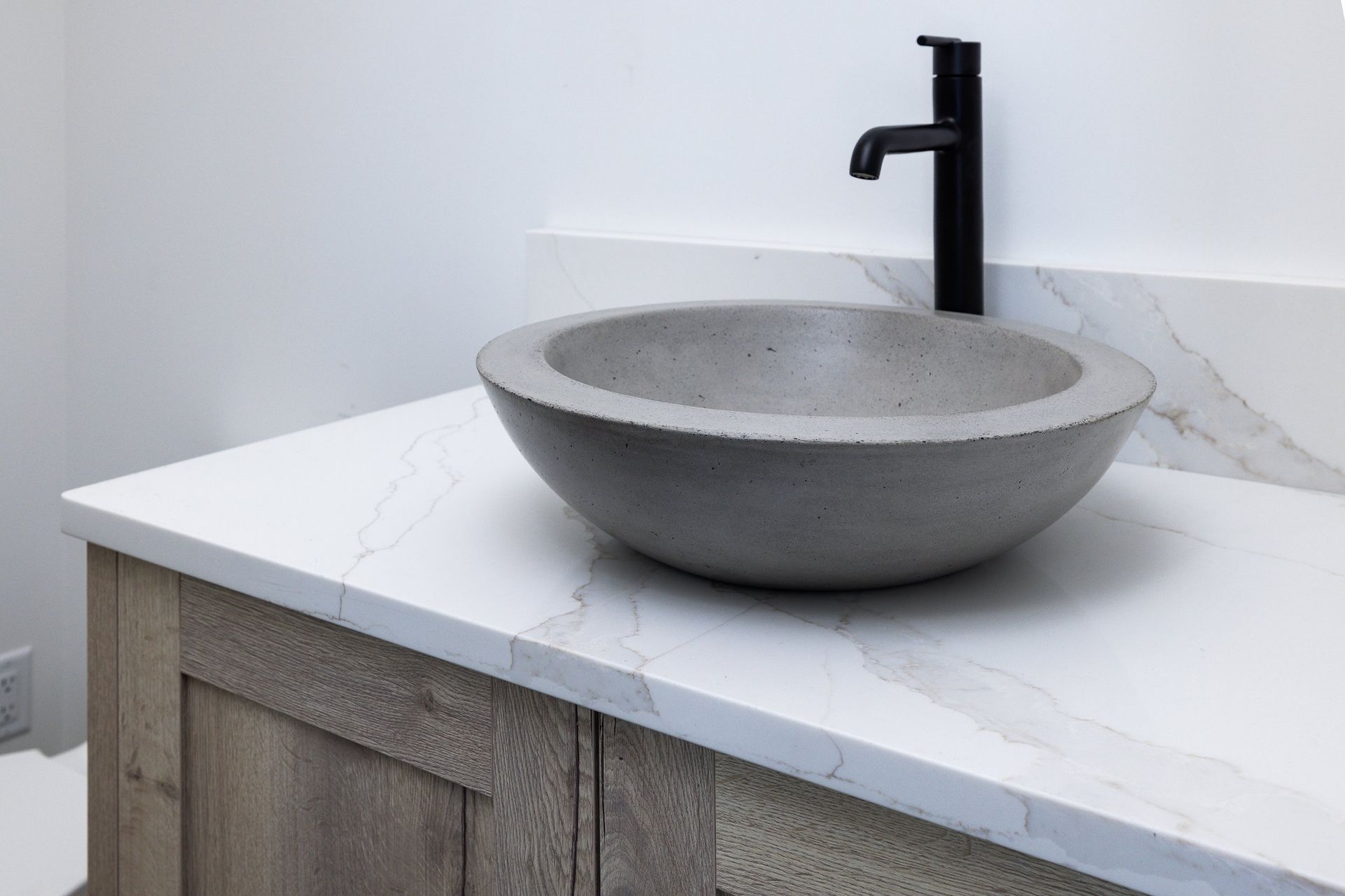 A gray concrete vessel sink sits on a white marble countertop with a black faucet in a modern bathroom.