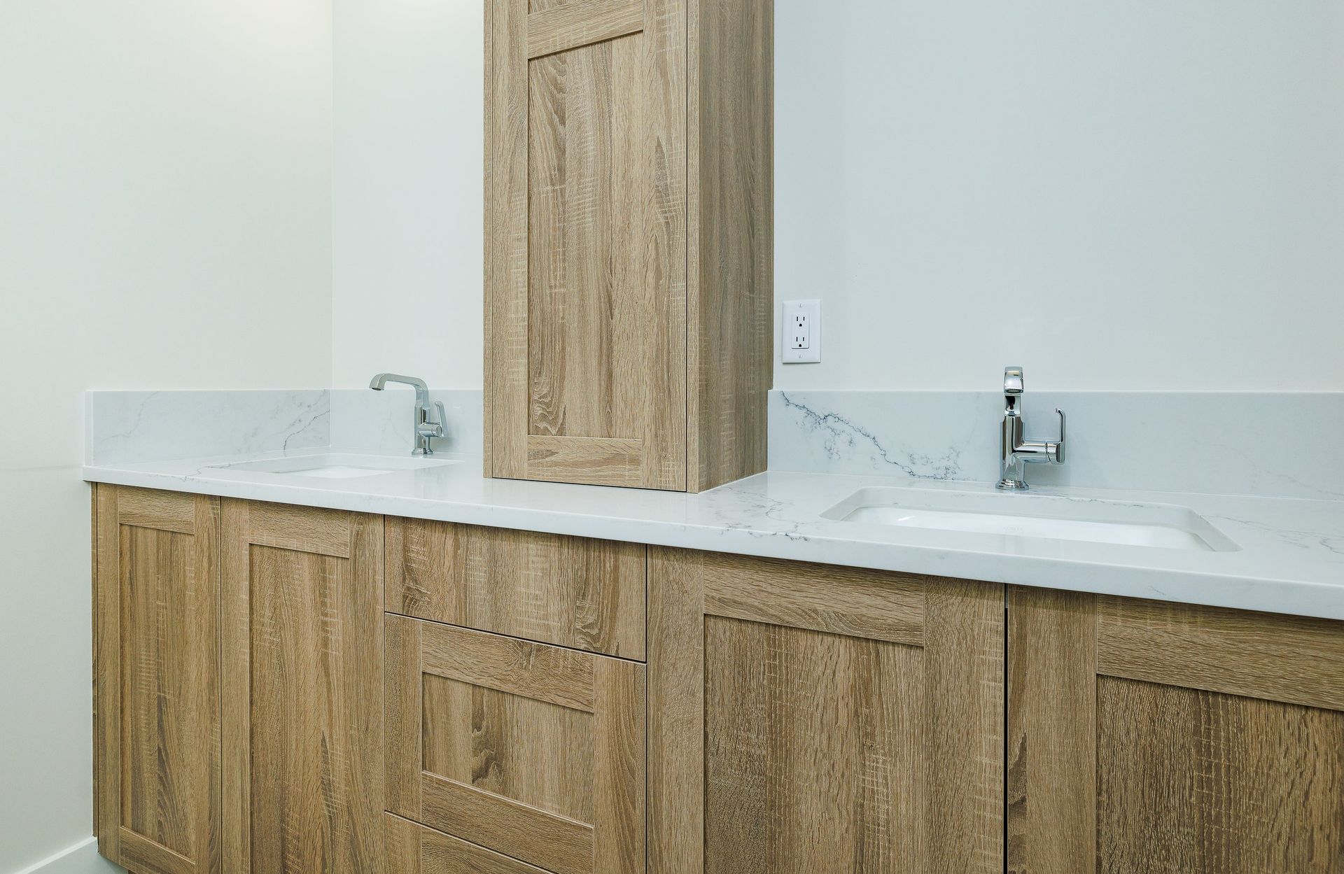 A double-sink bathroom vanity with light oak wood cabinetry, a white stone countertop, and two chrome faucets.