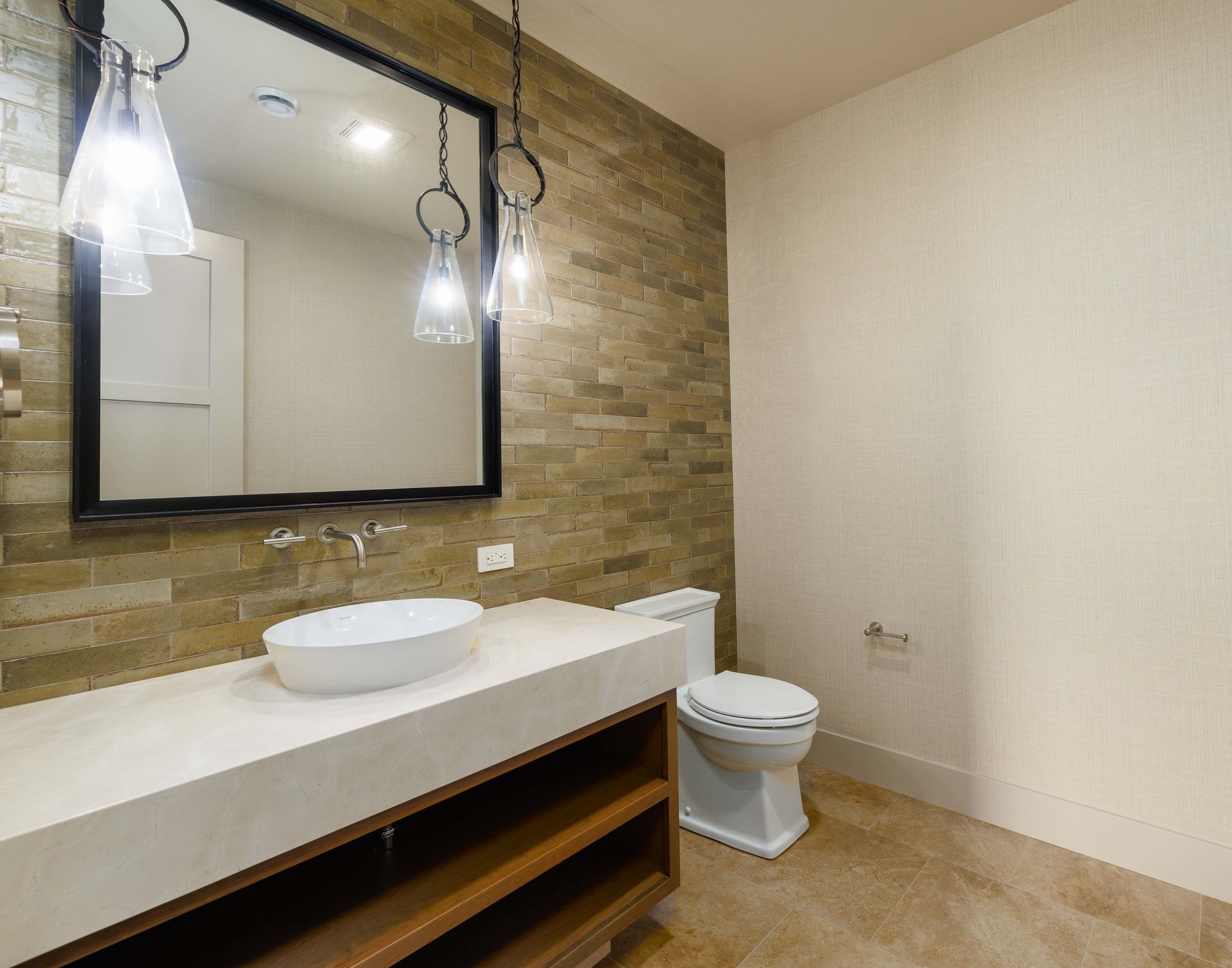 A modern bathroom with a stone tile accent wall, a floating wooden vanity, white vessel sink, and a toilet.