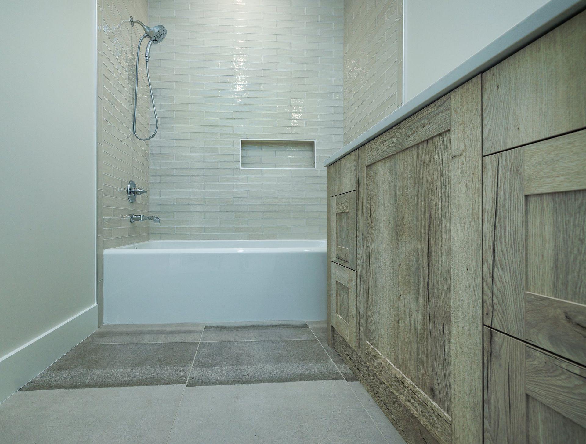 A modern bathroom featuring a white bathtub, beige textured wall tiles, and a light wood-grained vanity.