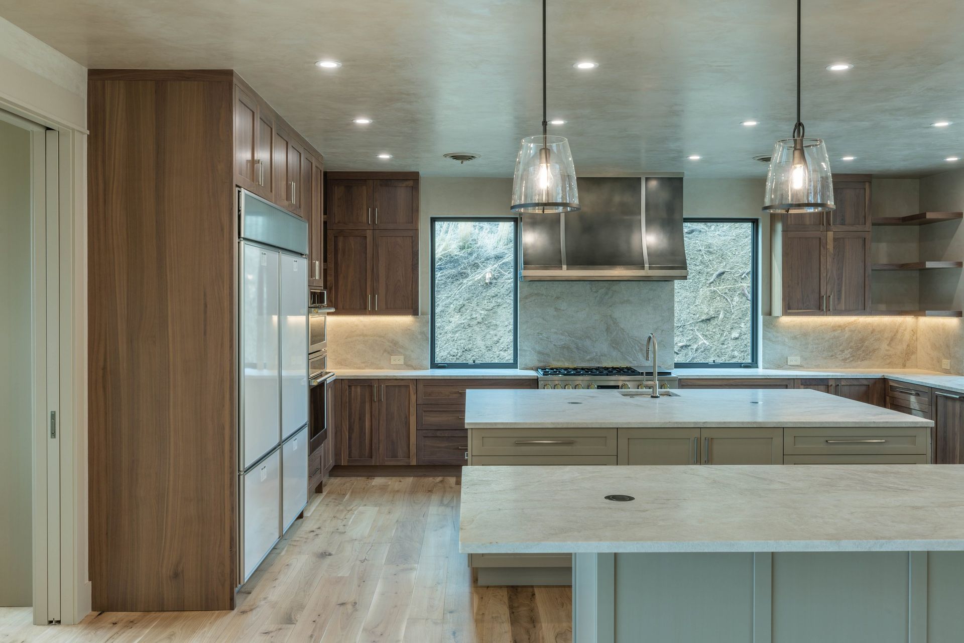 A modern kitchen featuring wood cabinetry, white countertops, two large islands, and two hanging pendant lights.