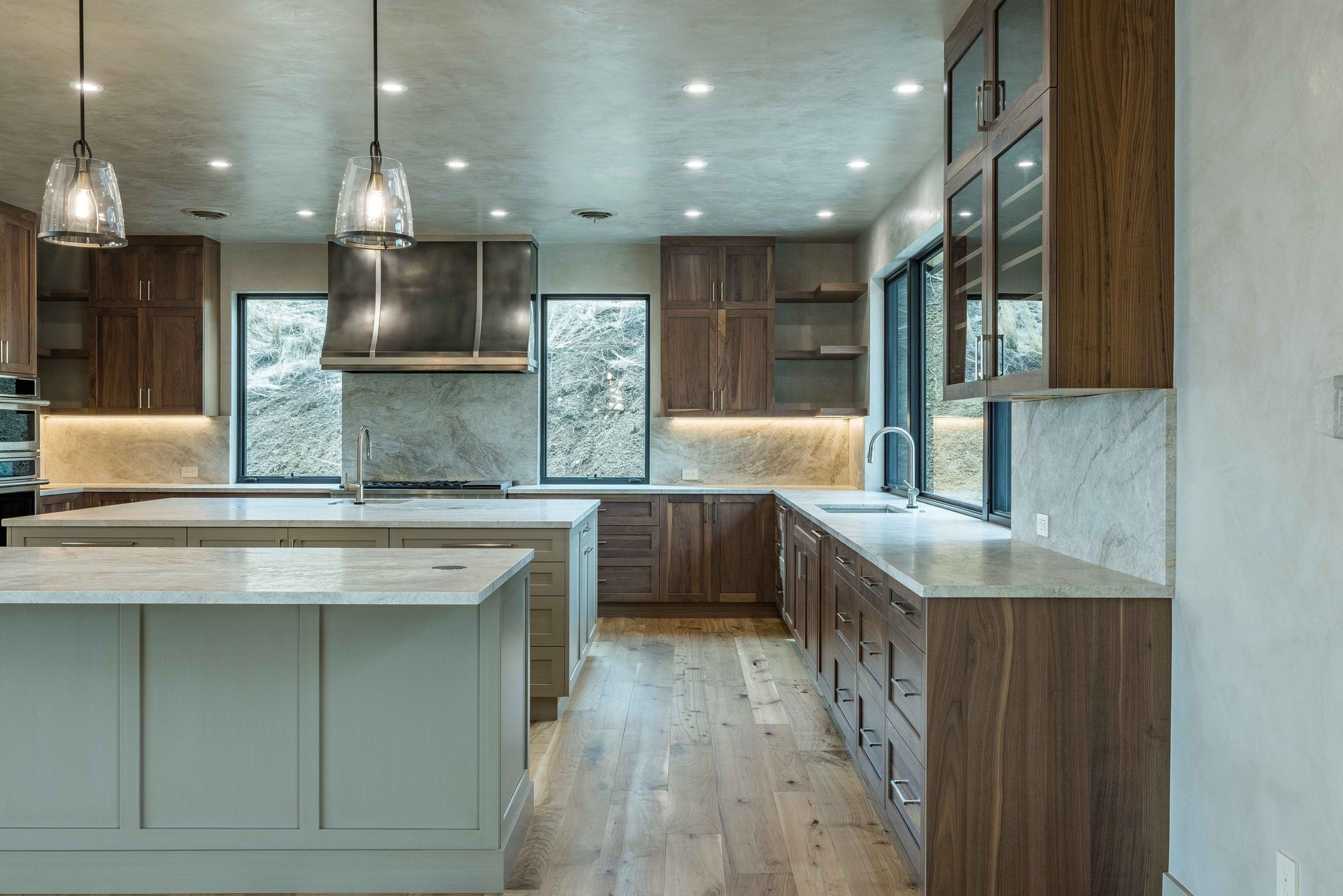 A modern kitchen featuring wood cabinets, light stone countertops, a large island, two pendant lights, and marble accents.