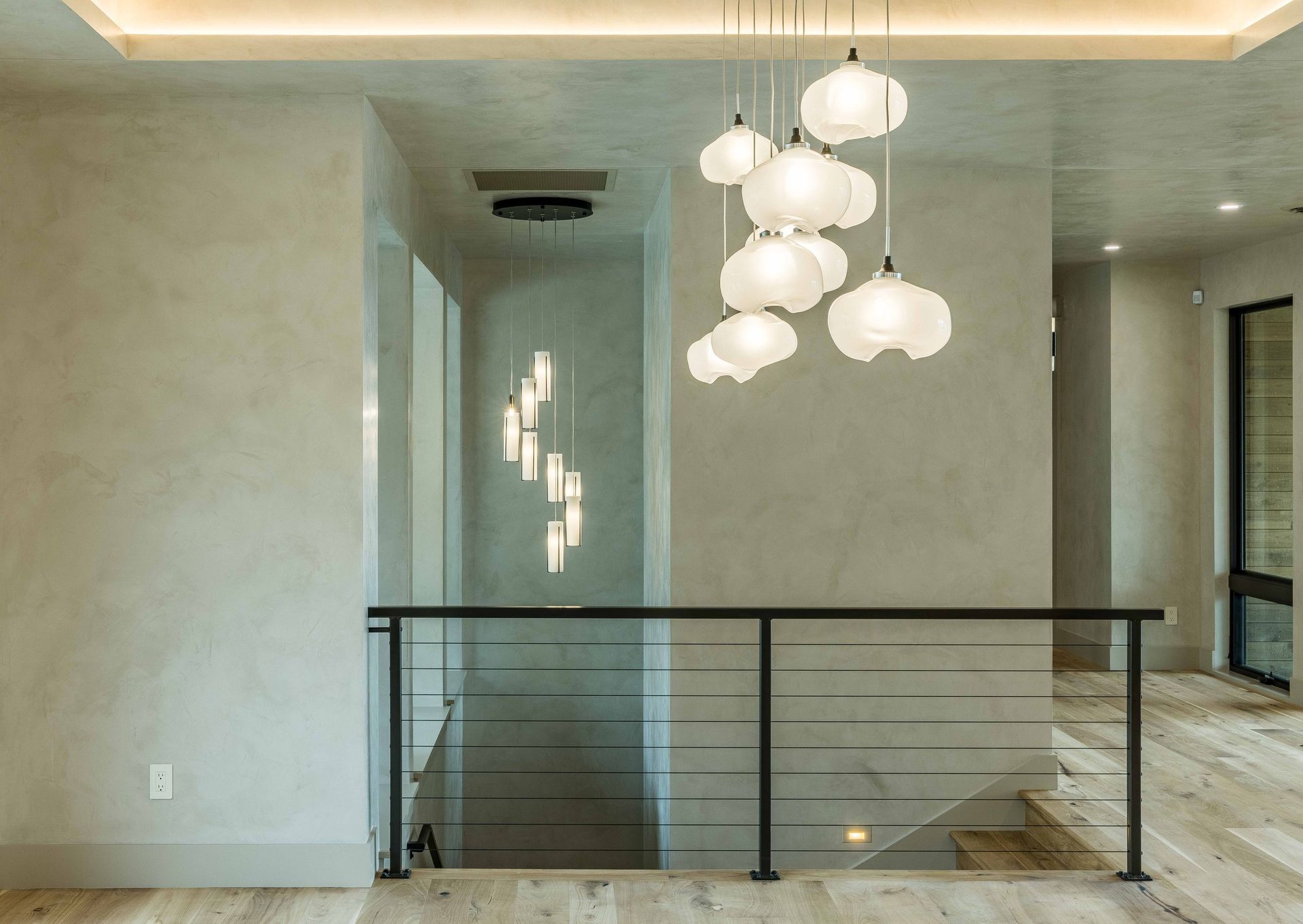 A modern staircase landing with soft-glow cloud-shaped pendant lights, neutral walls, and a black metal railing.