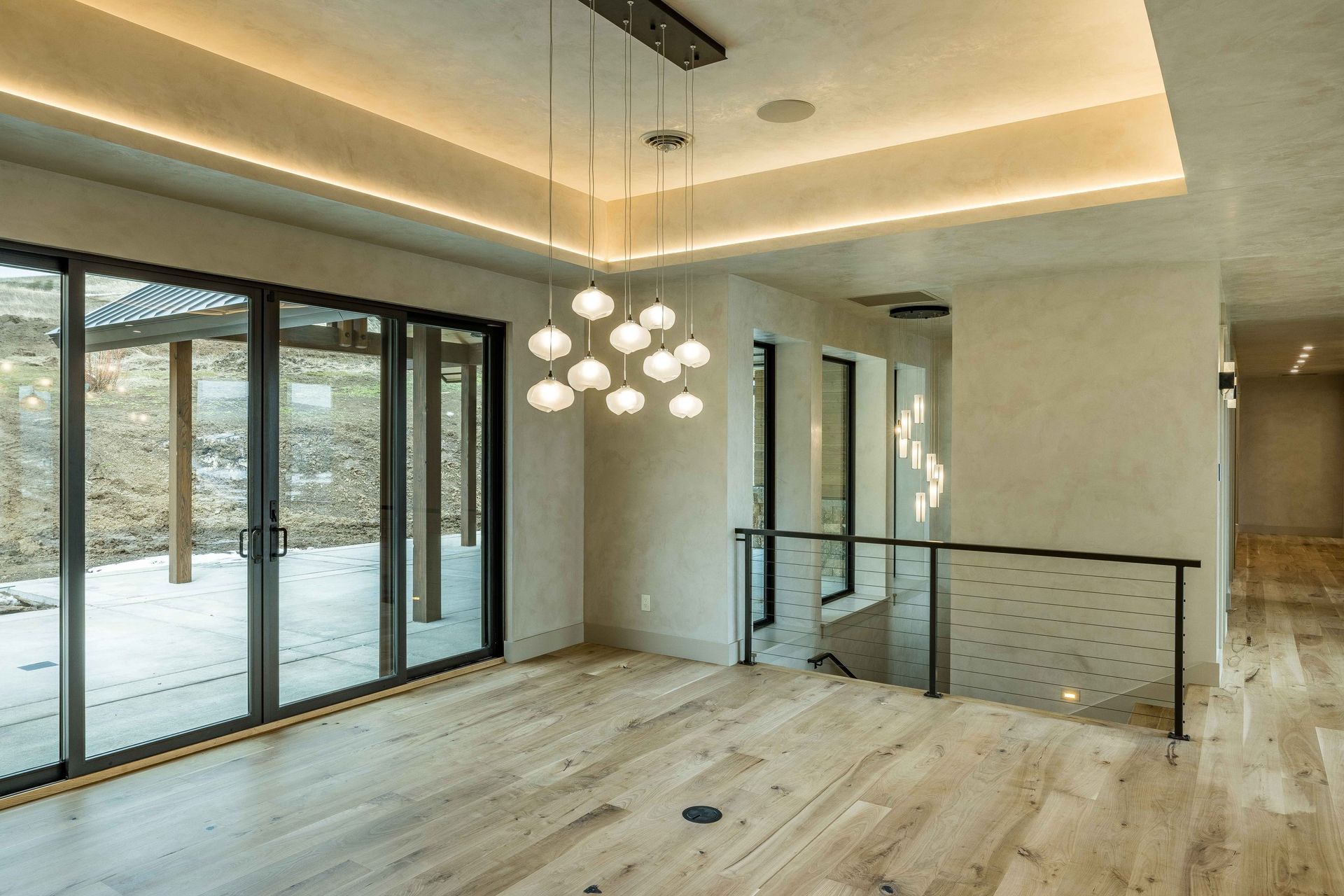 Modern interior space with light wood floors, a multi-globe chandelier, sliding glass doors, and a staircase railing.