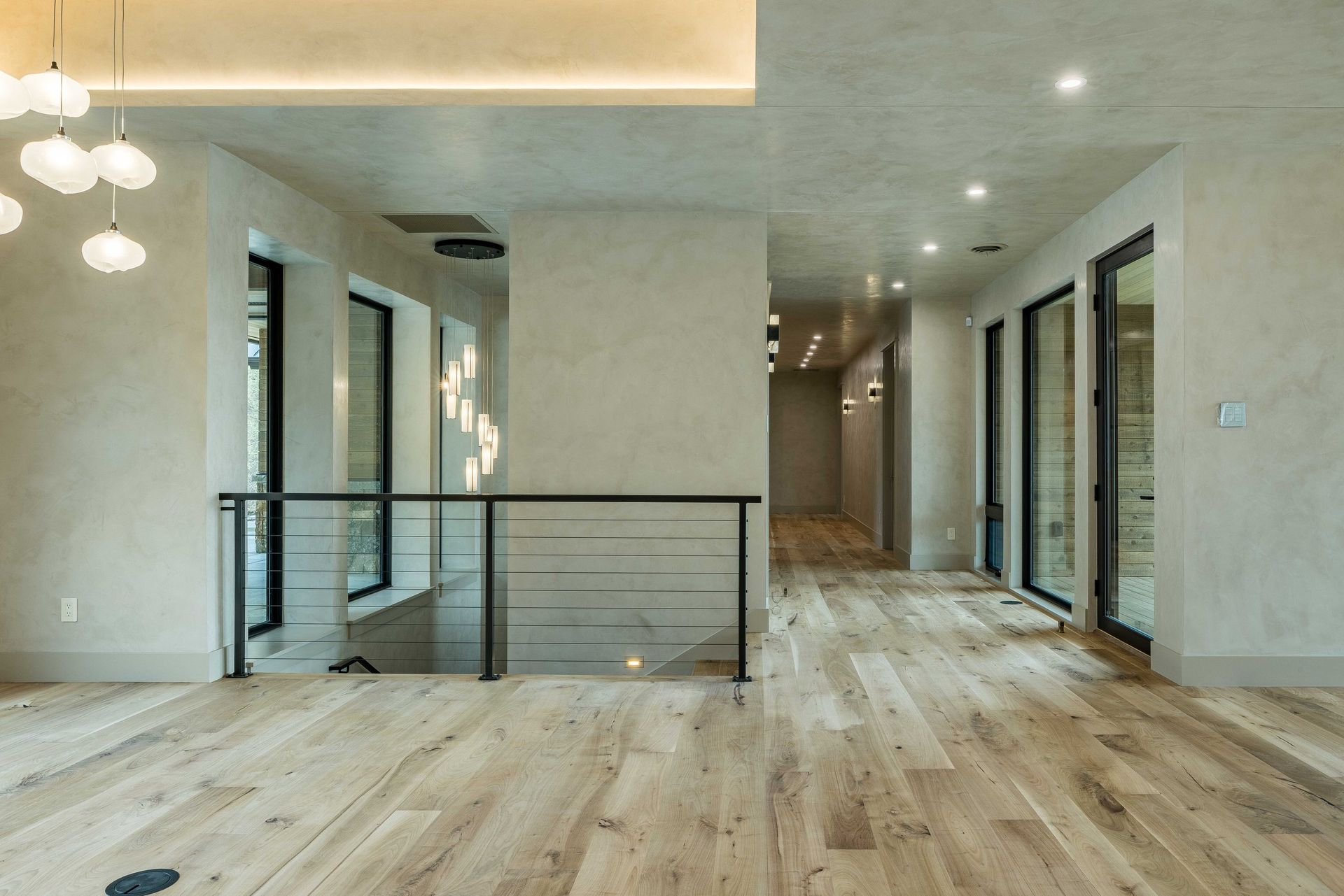 A bright, modern entryway with light wood floors, a black metal railing, and recessed ceiling lighting.