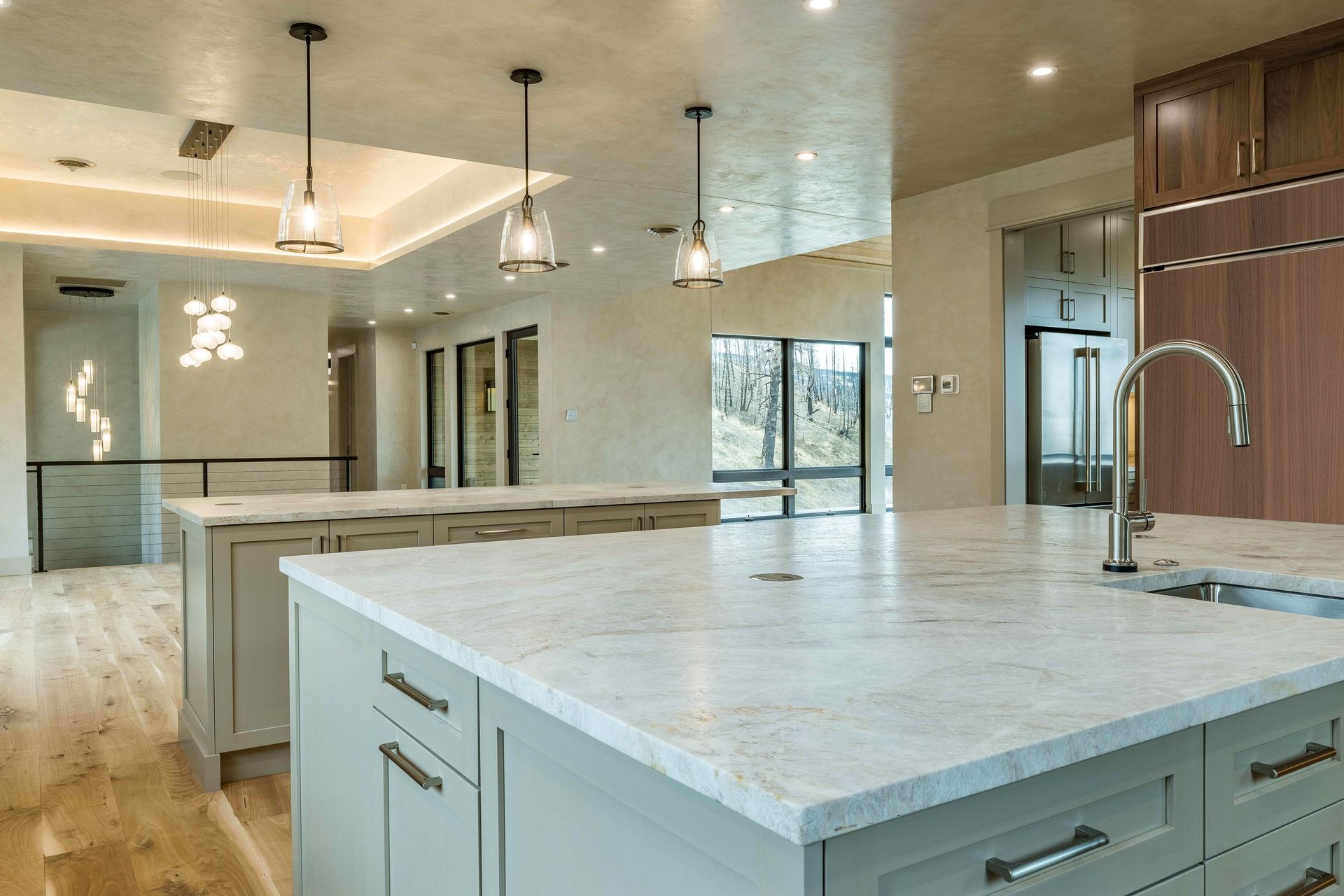 A bright modern kitchen with gray island cabinetry, light countertops, hanging pendant lights, and hardwood floors.
