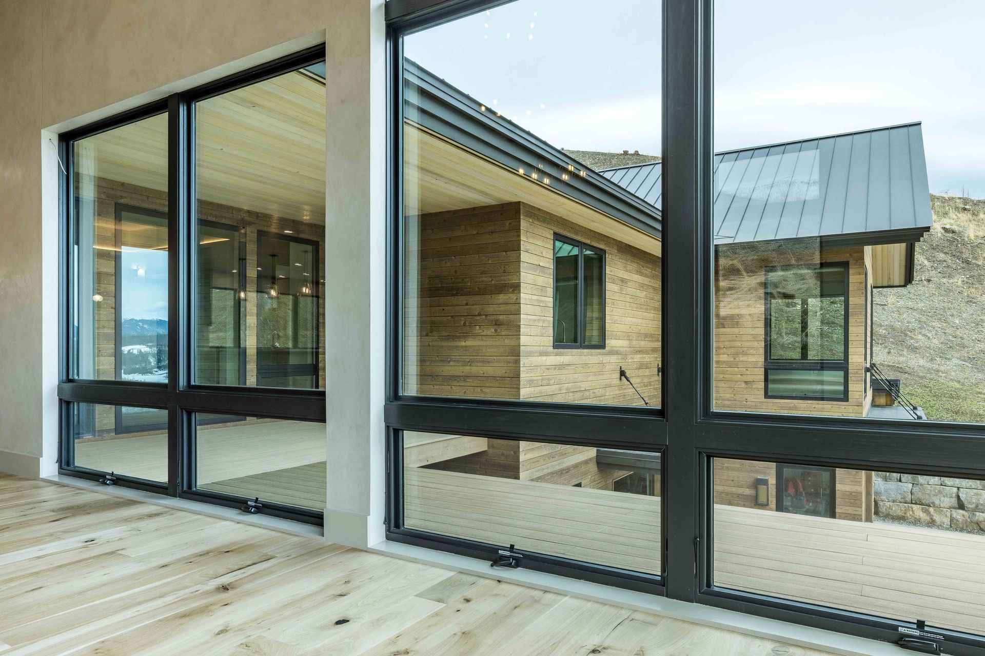 A modern room with large windows showing a wooden-sided house exterior and a landscape in the distance.