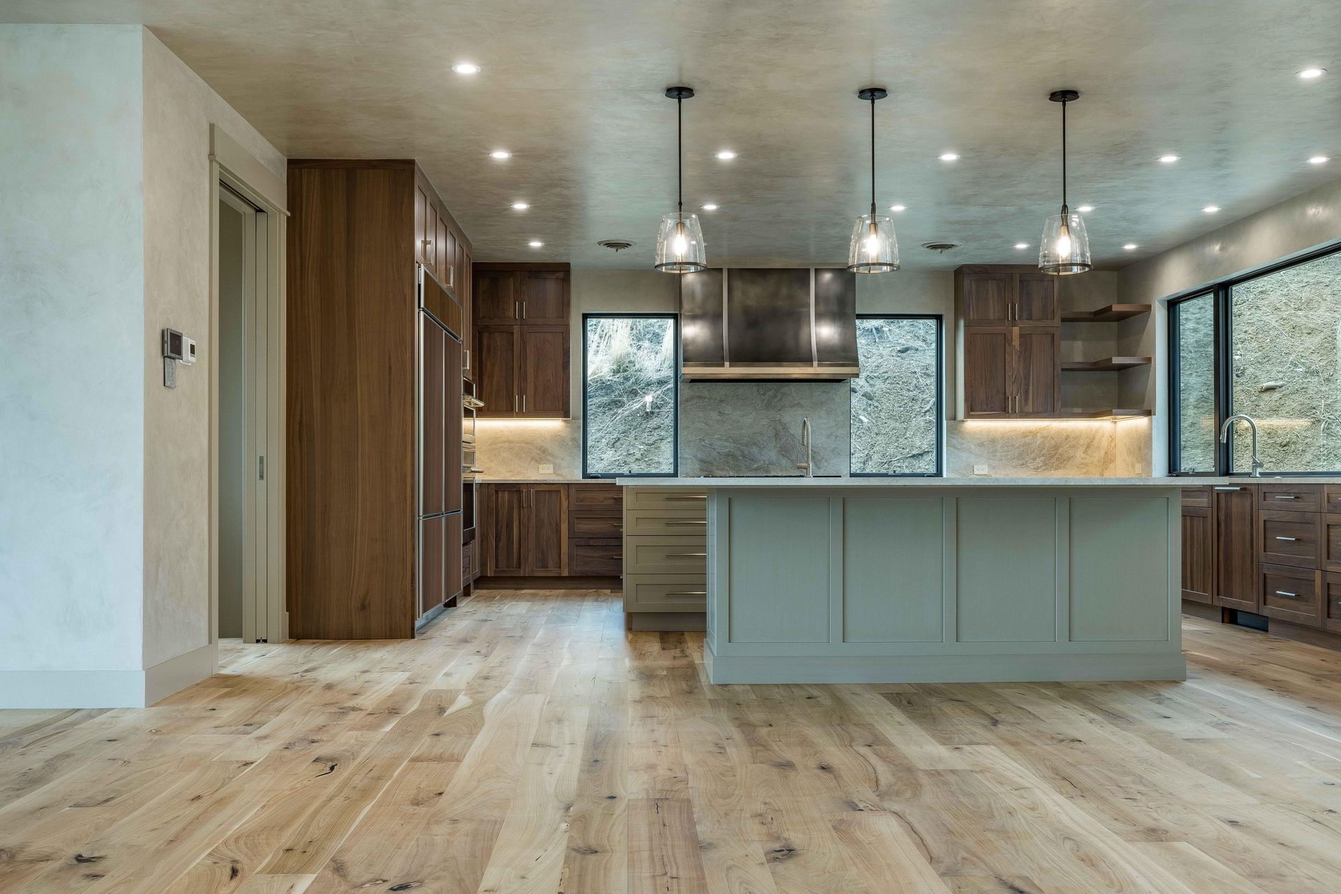 A modern kitchen with a grey island, walnut cabinets, white stone countertops, and three hanging pendant lights.