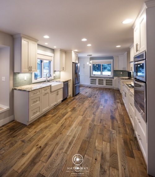 A spacious, modern kitchen featuring white cabinets, wood flooring, stainless steel appliances, and a farmhouse sink.