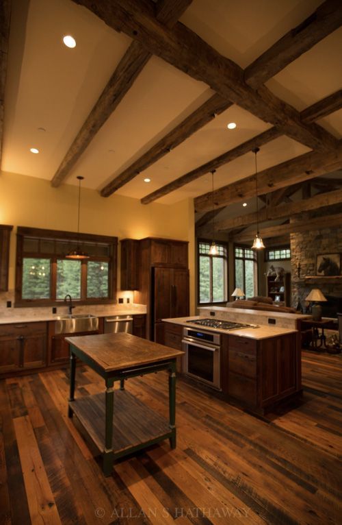 Rustic kitchen with dark wood cabinetry, exposed ceiling beams, hardwood floors, a center island, and a stone fireplace.