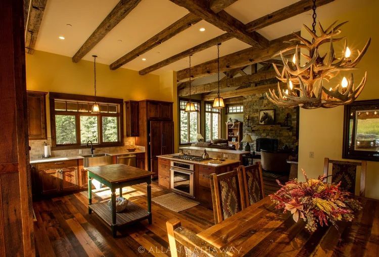 Rustic open-plan kitchen and dining area featuring wooden ceiling beams, antler chandelier, and warm-toned cabinetry.