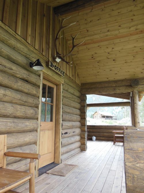A rustic log cabin porch featuring a wooden door labeled 