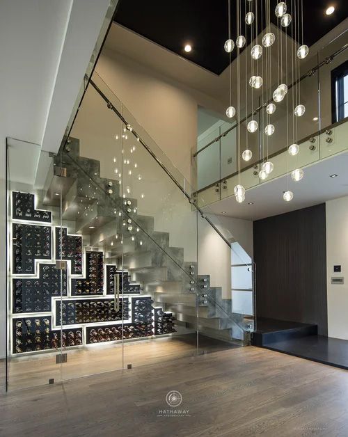A modern staircase with an integrated glass wine cellar below, a minimalist glass railing, and a hanging orb chandelier.