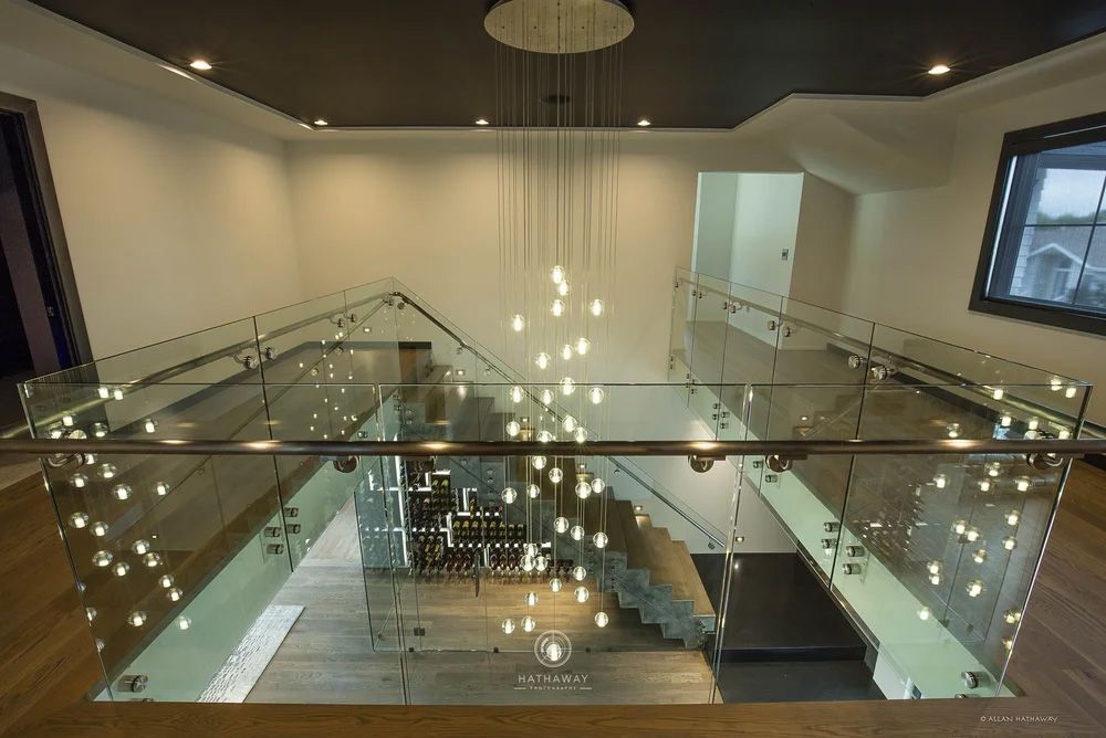 A modern staircase with glass railings and a multi-pendant chandelier in a bright, minimalist interior.
