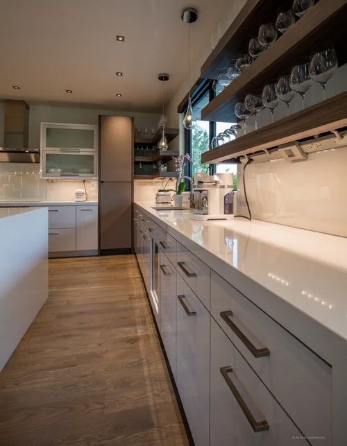 A modern kitchen with white cabinets, wood flooring, and open shelving featuring hanging wine glasses.