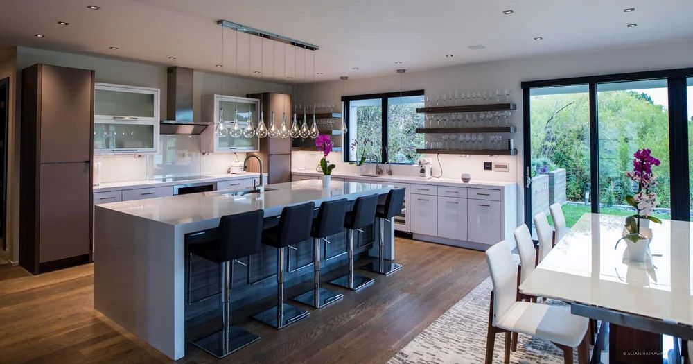 A modern kitchen with a large island featuring black stools, white cabinets, and an adjacent dining area.