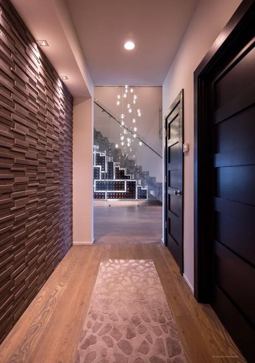 A hallway with a textured dark wall, wooden floors, a patterned runner, and a lit staircase with hanging lights.