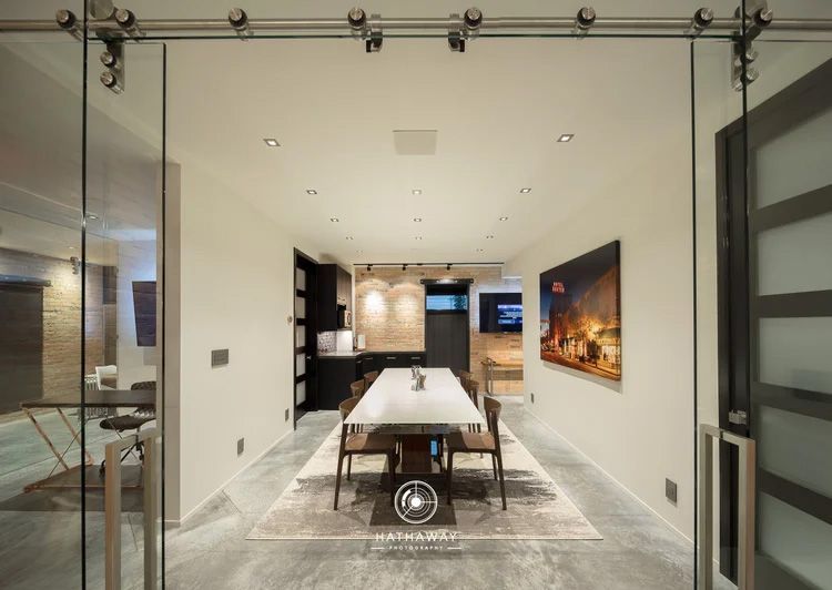 Modern dining room seen through glass sliding doors, featuring a white table, chairs, and large art on a neutral wall.