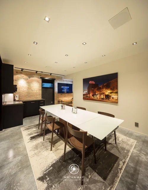 Modern conference room with a long white table, wooden chairs, polished concrete floors, and a brick accent wall.