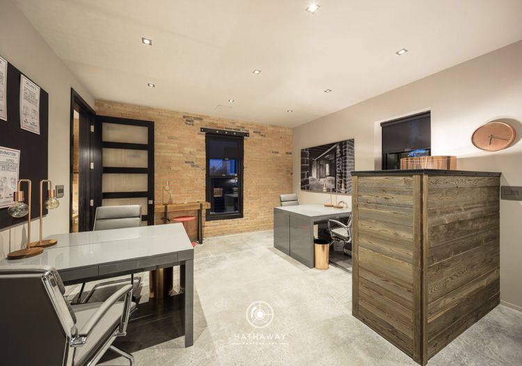 Modern home office featuring a light-colored wood paneled wall, concrete floors, gray desks, and recessed lighting.
