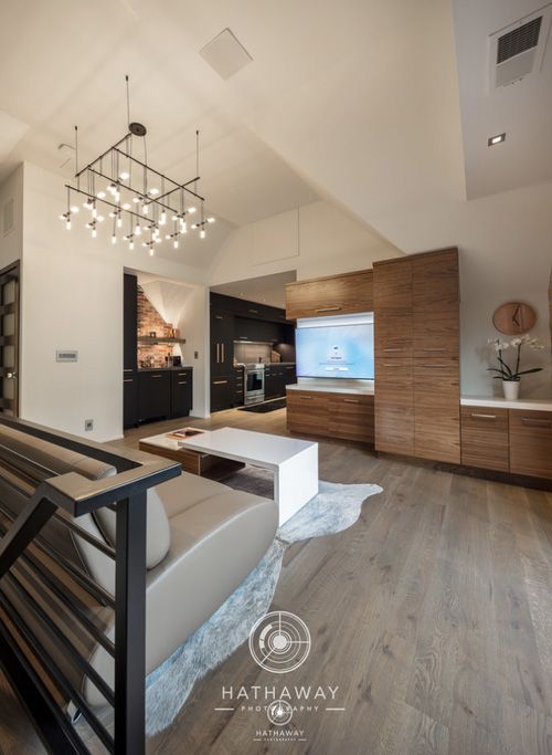 A modern living room with wood cabinetry, a mounted television, a gray sofa, and a large, multi-bulb chandelier.