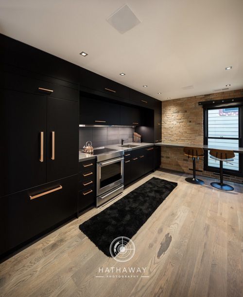 Modern kitchen with matte black cabinetry, light wood floors, a brick accent wall, and a black runner rug.