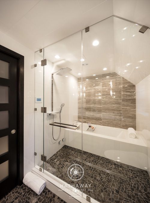 Modern bathroom with a glass-enclosed shower and tub featuring dark stone flooring and grey tiled walls.