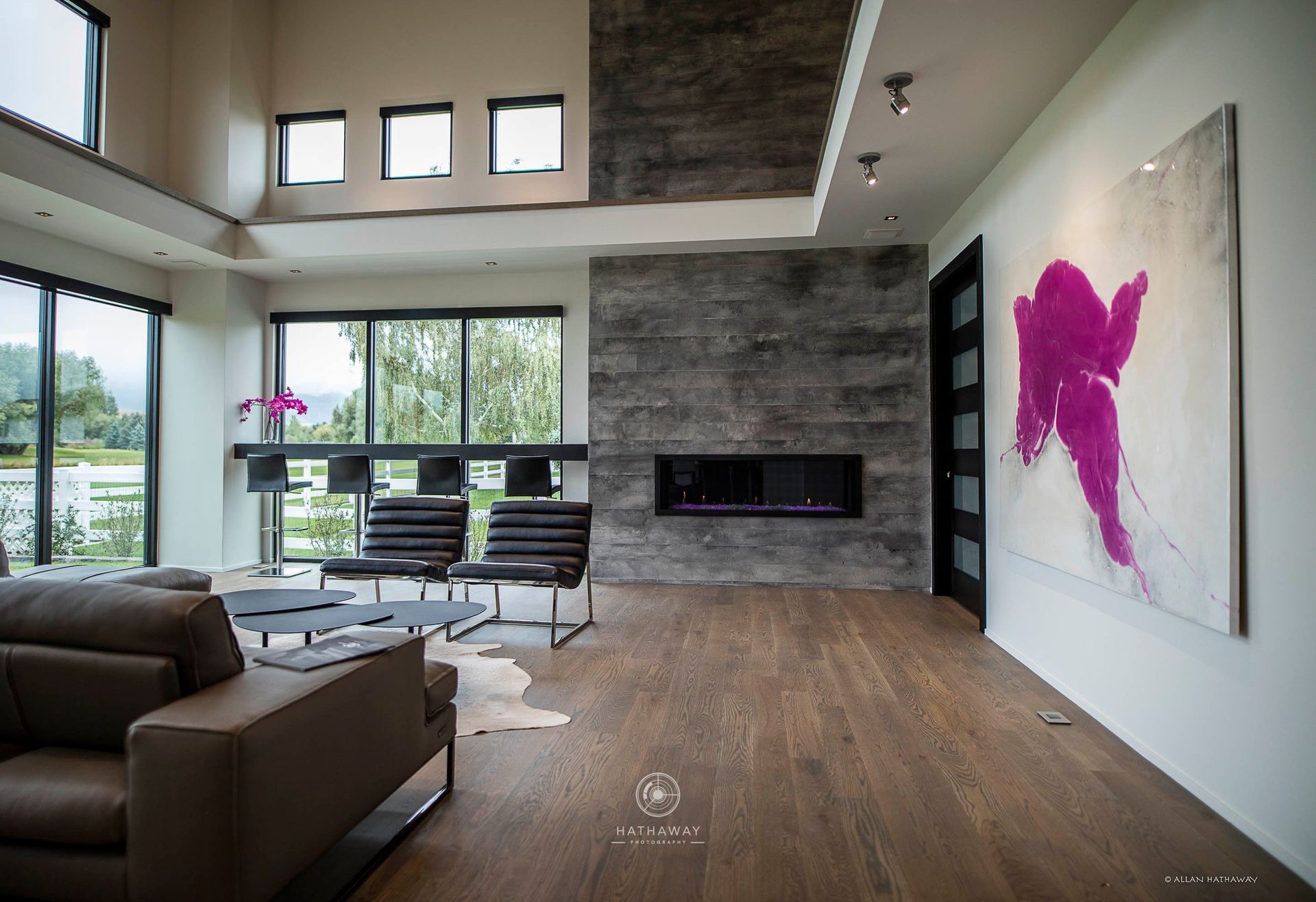 Modern living room with a large stone fireplace, brown leather sofa, two black chairs, and a large abstract fuchsia painting.