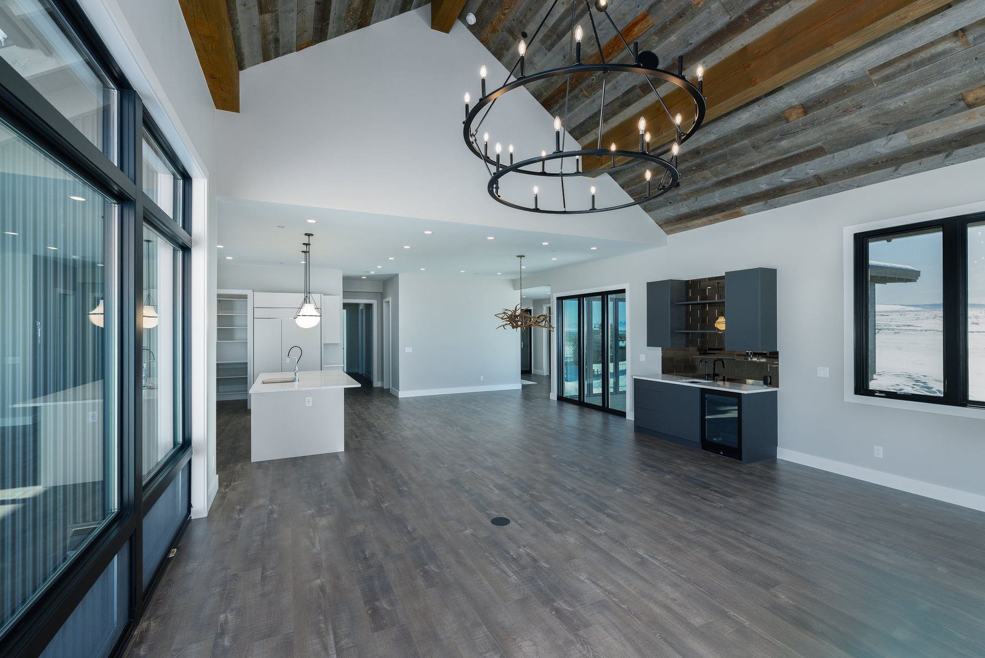 A modern open-concept living area with wood-beamed ceilings, a chandelier, white kitchen island, and gray cabinetry.