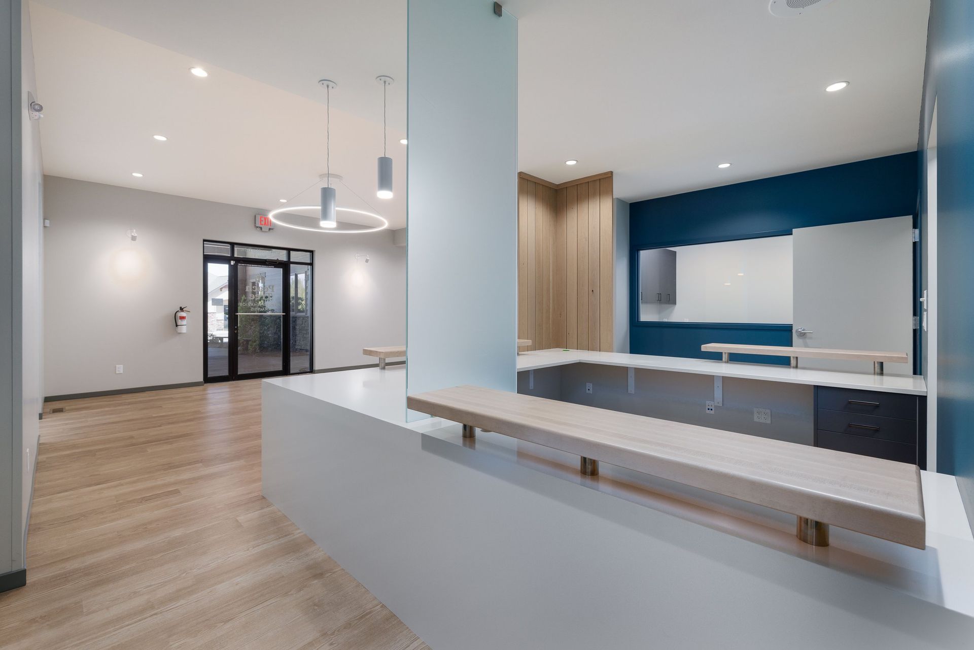 Modern reception area with a white service counter, light wood flooring, and blue accent wall in a bright, open office.