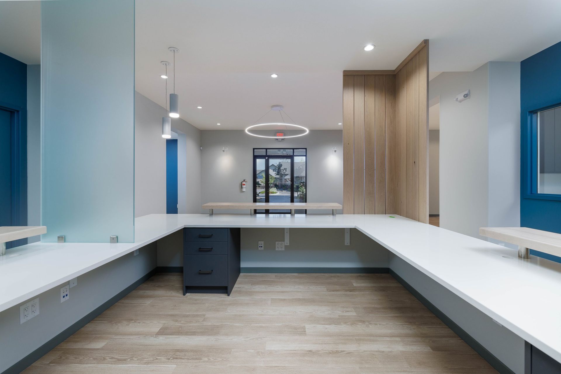 A modern, U-shaped white reception desk with a black drawer unit sits in an office space with blue walls and wood accents.
