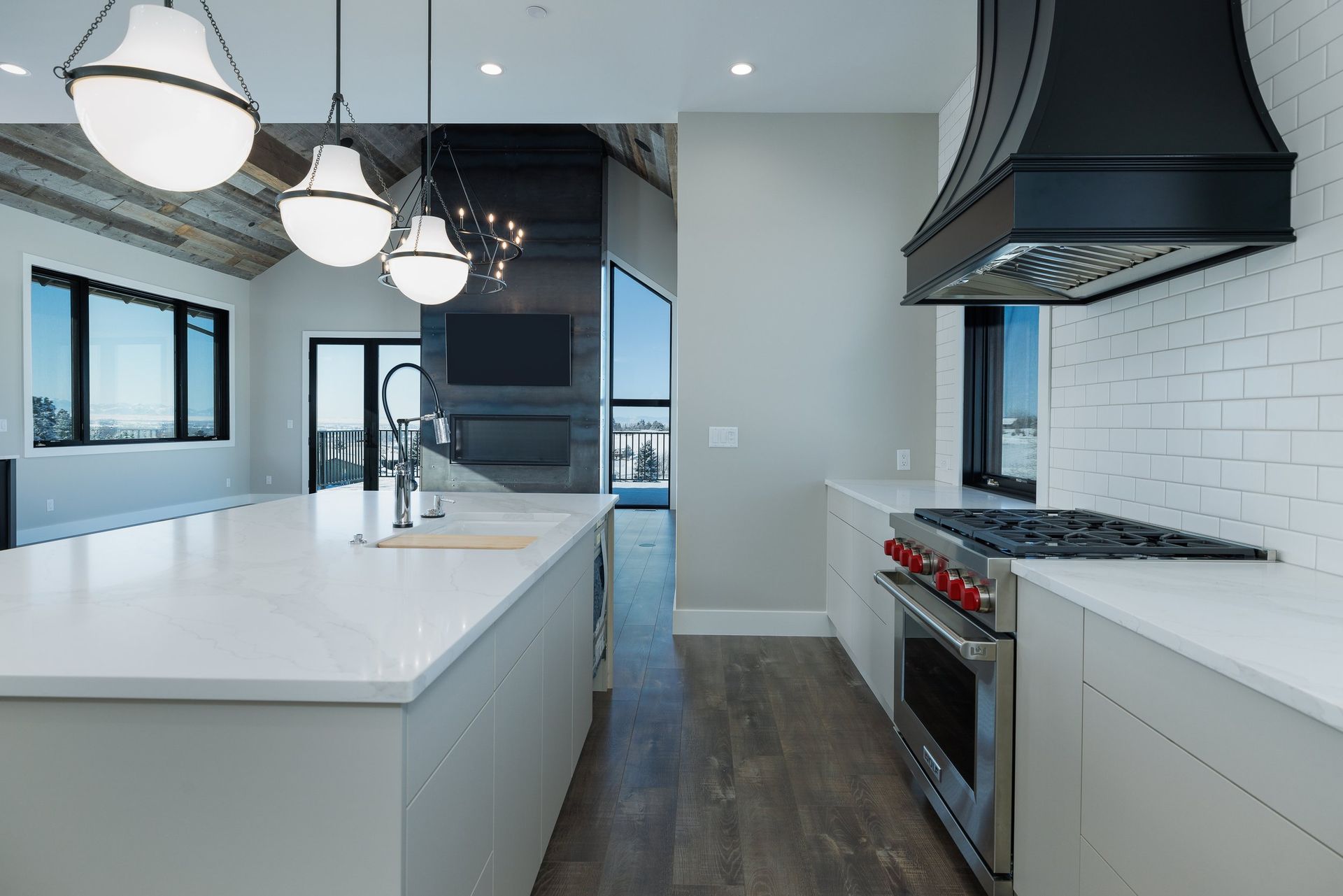 A modern, bright kitchen featuring a white island, pendant lighting, stainless steel stove, and a black range hood.